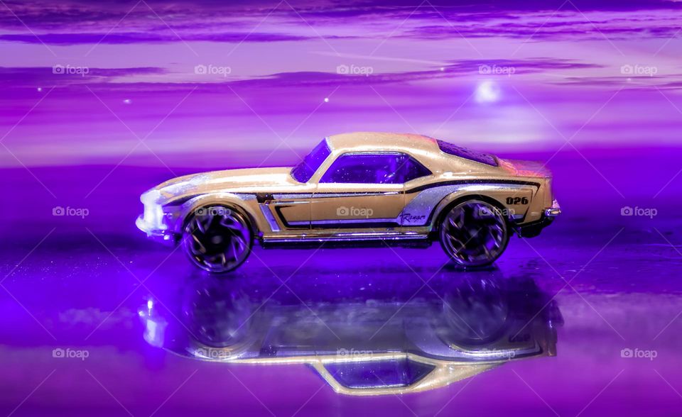 A gold car drives on a wet road under purple twilight skies - a composite of a toy car, shot with purple lighting and reflected on glass with clouds added from another image that I took, which has also been entered into this mission.
