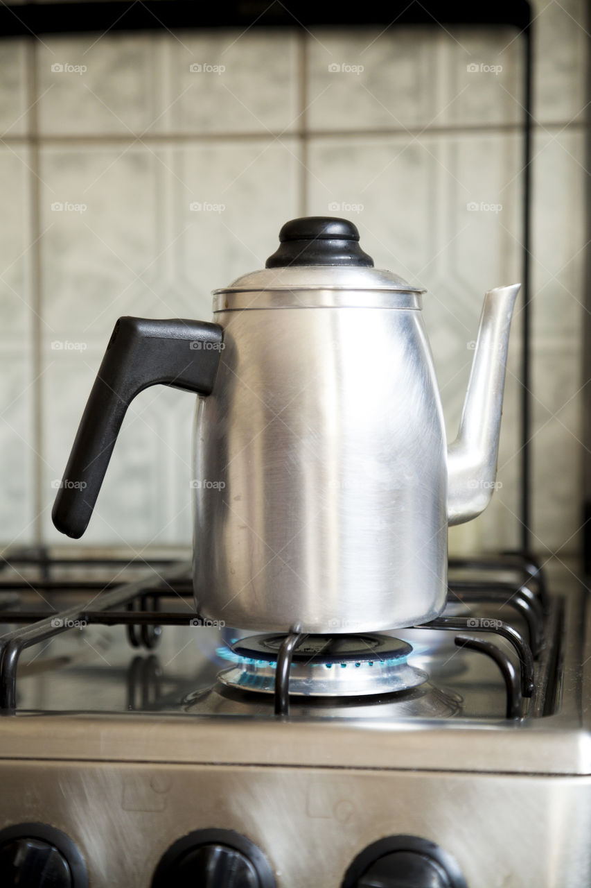 Coffee pot being heated on a residential stove over a low flame in a Brazilian house. Textured tile background in Brazilian cuisine. Copy space. Drink concept. Coffee concept.