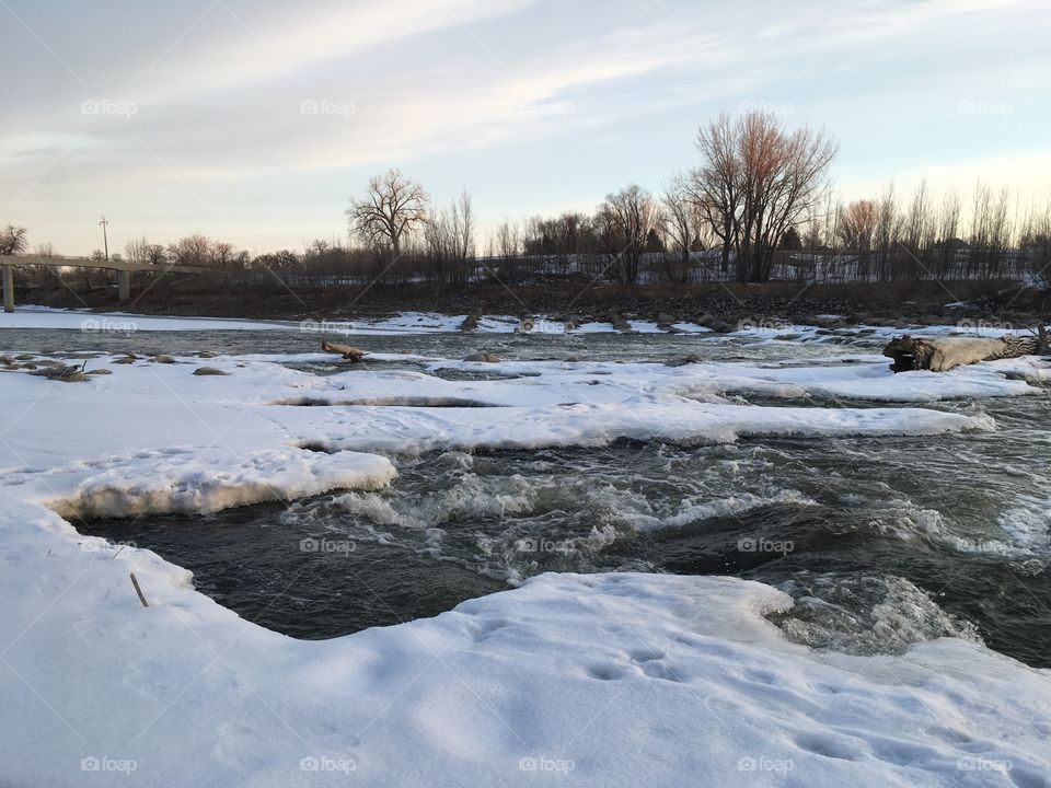 Beautiful dawn over the red river. There’s a hint of tree as the sun rises over the river and everything is icy. Flowing water.