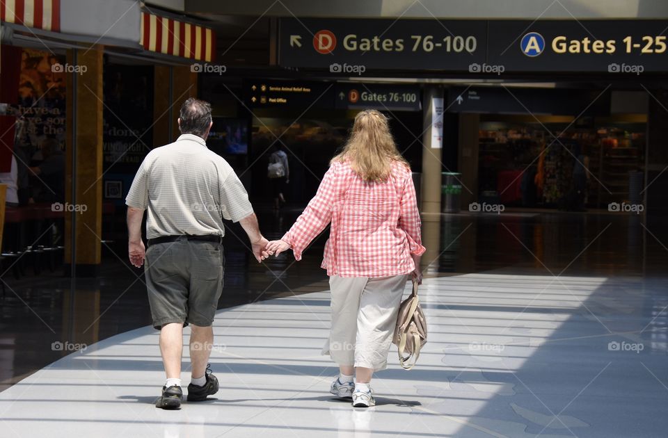 A couple walking through airport holding hands, sunlight shining on them