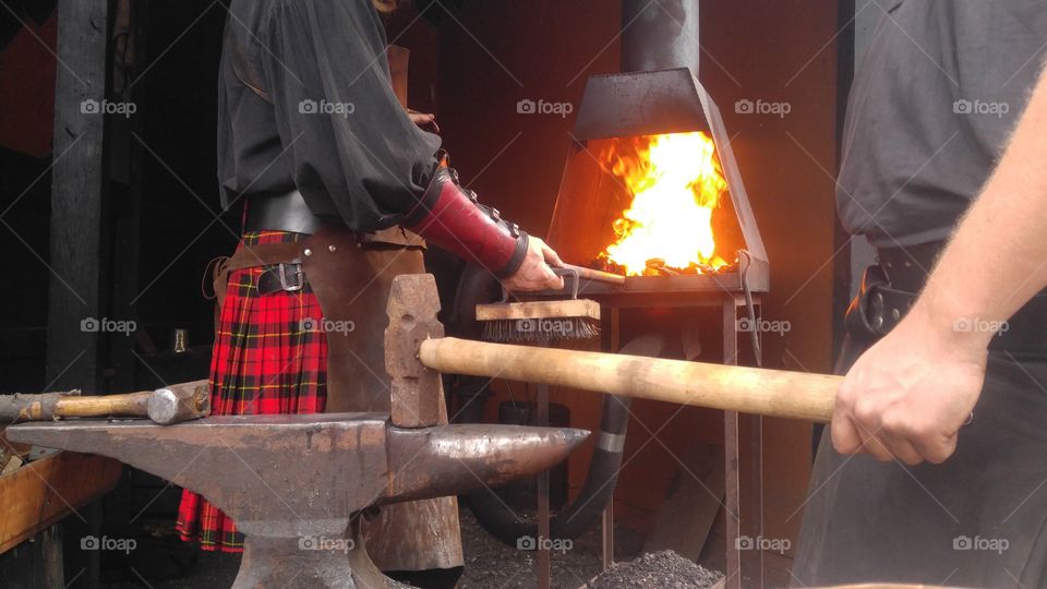 The apprentice (in this case taking on the role of the striker) waits beside the anvil with his hammer for the blacksmith to remove the Iron rod. Then they work in unison to shape the metal, by alternating strikes.
