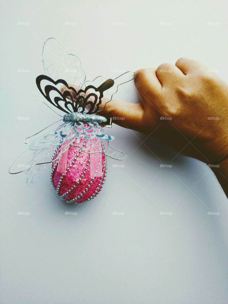 Minimalist photo holding pink decorative egg work a silver butterfly