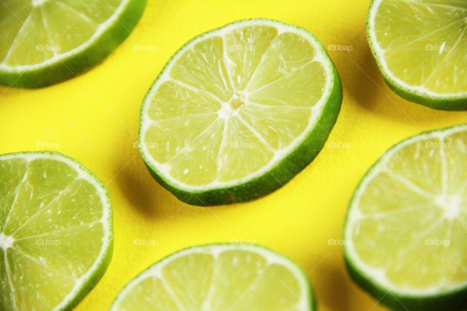 Close up de limón en fondo amarillo, rodaja circulares de limón cortada contrastando sobre un fondo amarillo fuerte, un detalle que resalta la textura en el limón.