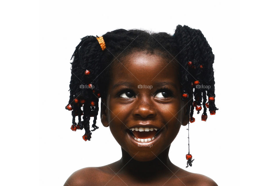 A young african child toothy smiling infront of a white backdrop and in dreadlock.