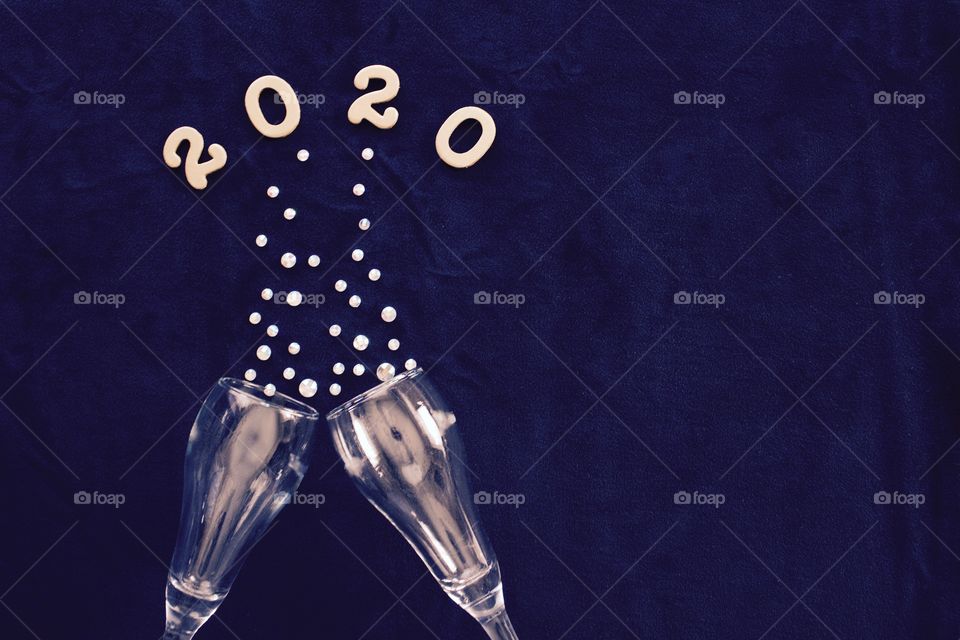 Flat lay of the numbers ‘2020’ above champagne glasses with rhinestone bubbles on classic blue background - copy space on right side of landscape format