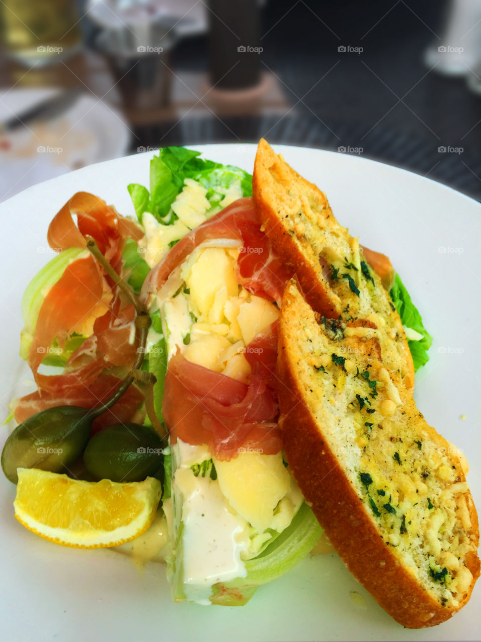 Closeup of a de-constructed Caesar salad. A wedge of romaine, prosciutto, fresh parmesan flakes, huge fresh capers, super garlicky toast croutons, a slice of lemon and some fresh house-made dressing. Yumm!