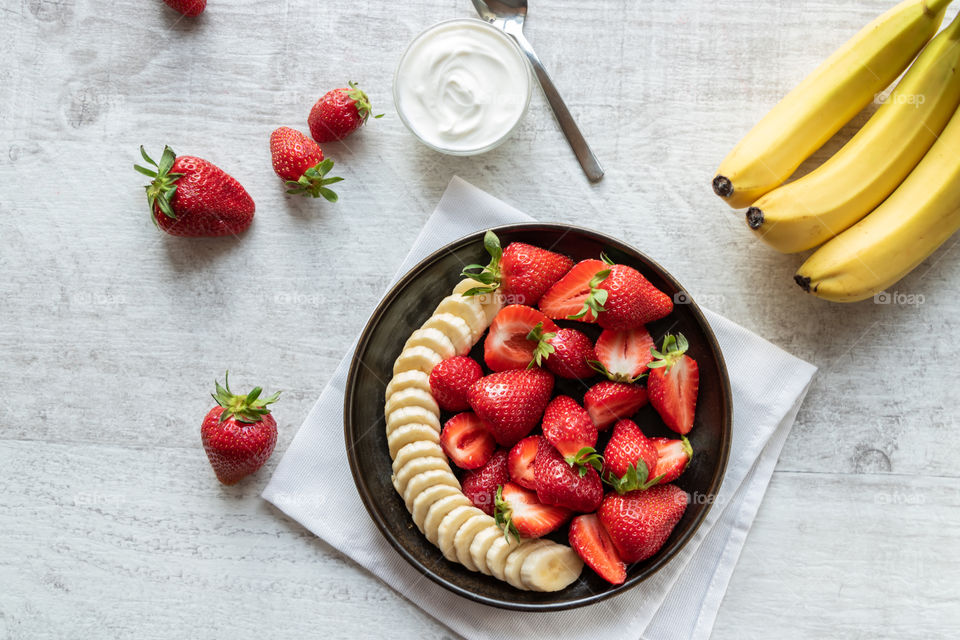 Top view of strawberries and banana salad on wooden table. Concept of healthy lifestyle.