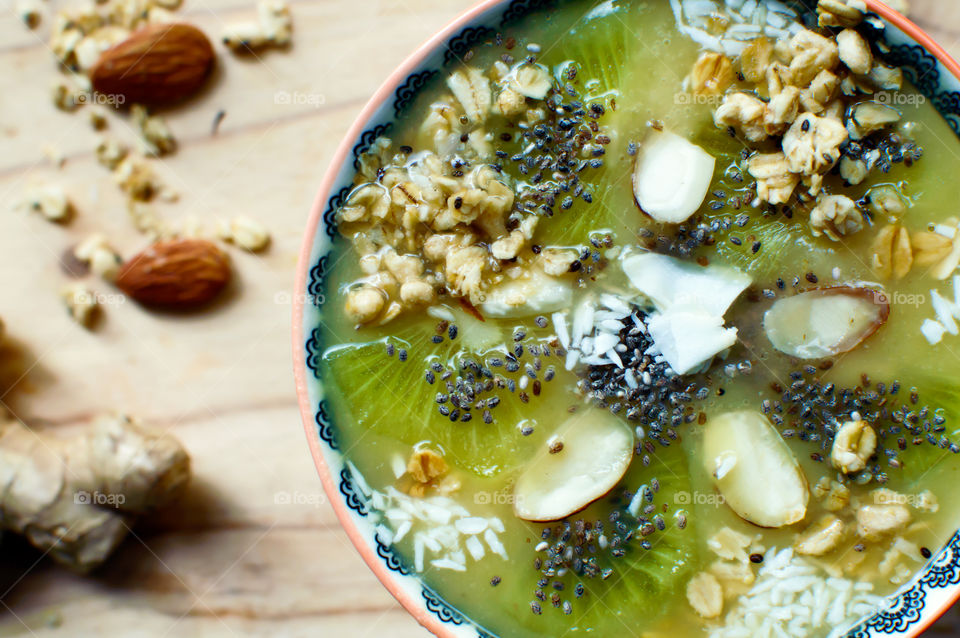 Close-up fresh healthy fruit smoothie bowl with ginger, chia seed, almond, kiwi, coconut and oatmeal in mandala design elevated view green and white colors