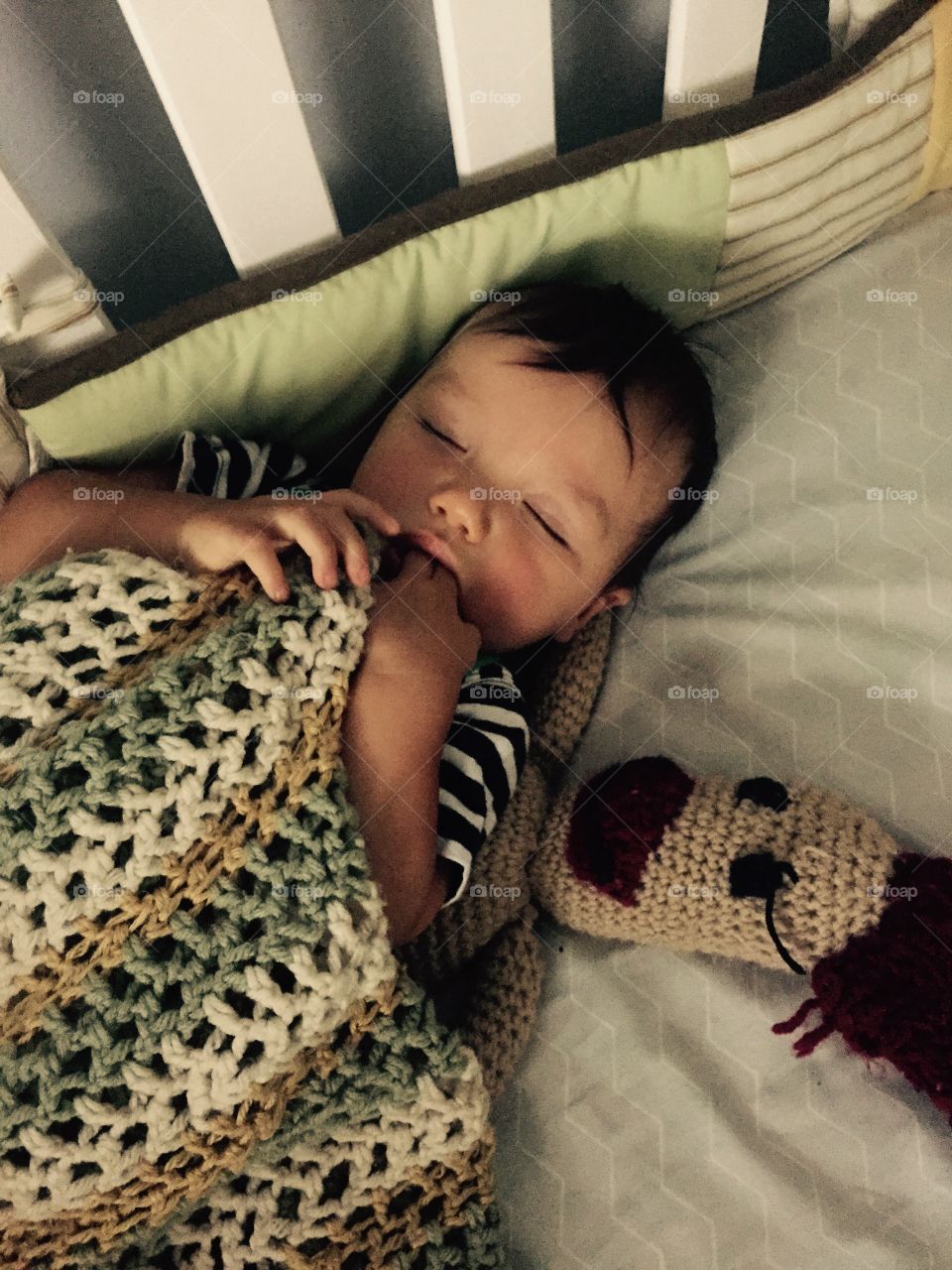 Our 9 month old grandson, sleeping in his crib with the crocheted yellow, sage green , and cream blanket Grammie made him.