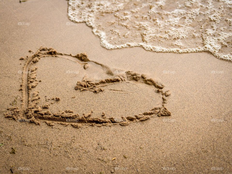 Heart drawn in sand being washed away