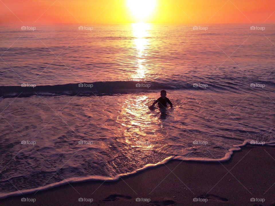 Small boy in the ocean during a magnificent sunset.