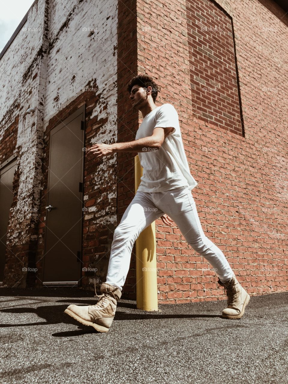 A young man walking down the street wearing white clothes.  Cool, urban city vibe.