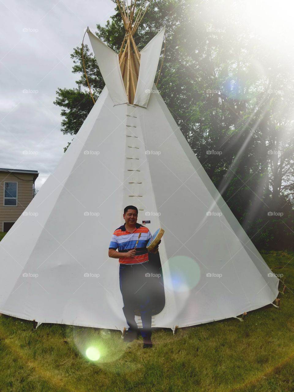 indigenous man drums in front of a teepee constructed as a classroom for indigenous students.