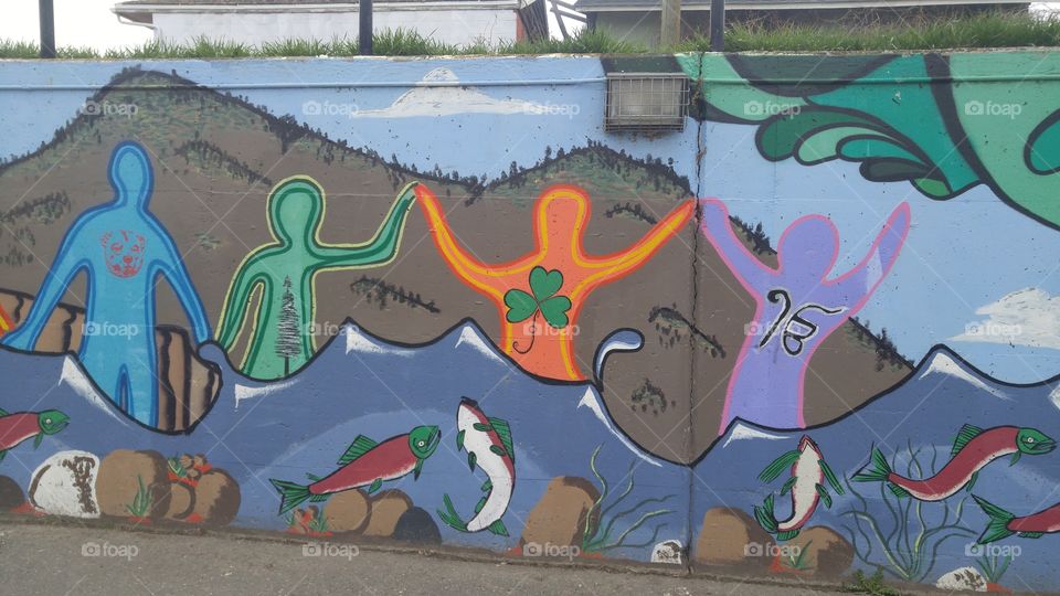 Section of parking lot wall art showing symbolic people by local mountains and river with sockeye salmon spawning.