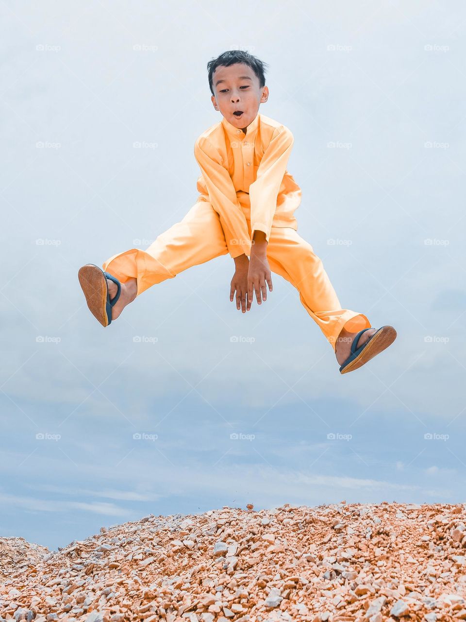 A boy in yellow jumping on sand dunes on a sunny day