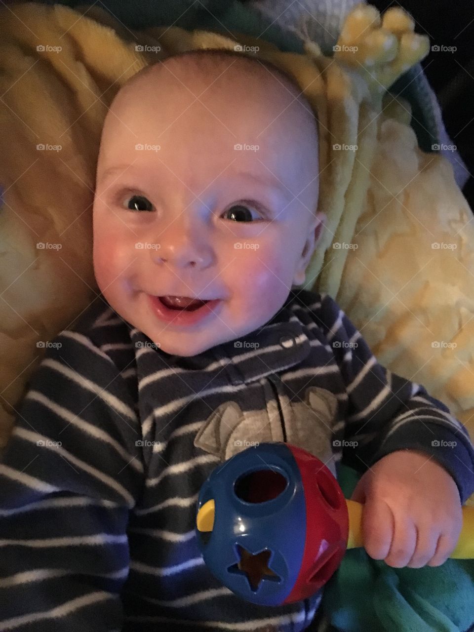 Smiling baby lying in bed and holding toy