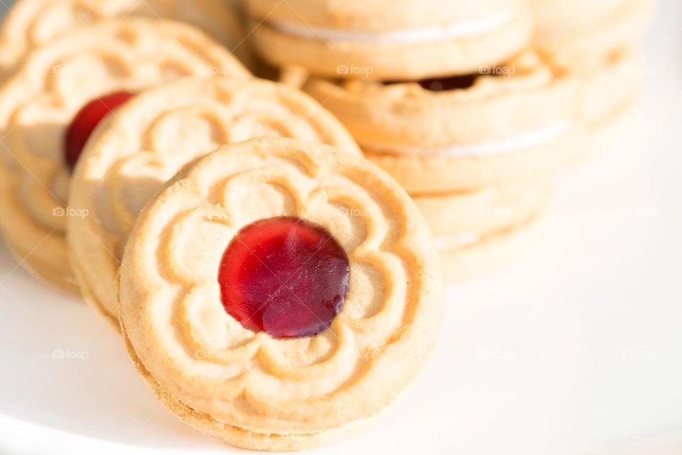 Closeup of vanilla biscuit cookies with raspberry jam in the middle on a white plate 