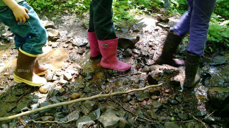 kids in rubber rain boots hiking through a creek