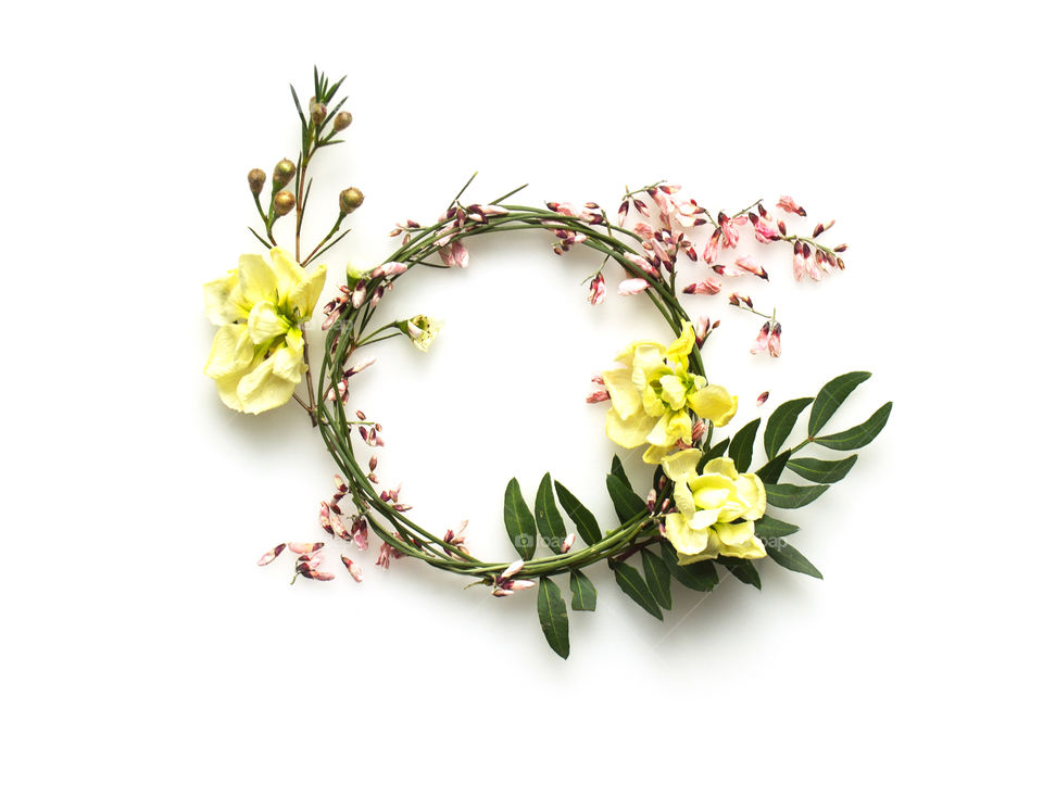 Round frame made of pink and yellow flowers, twigs and leaves 