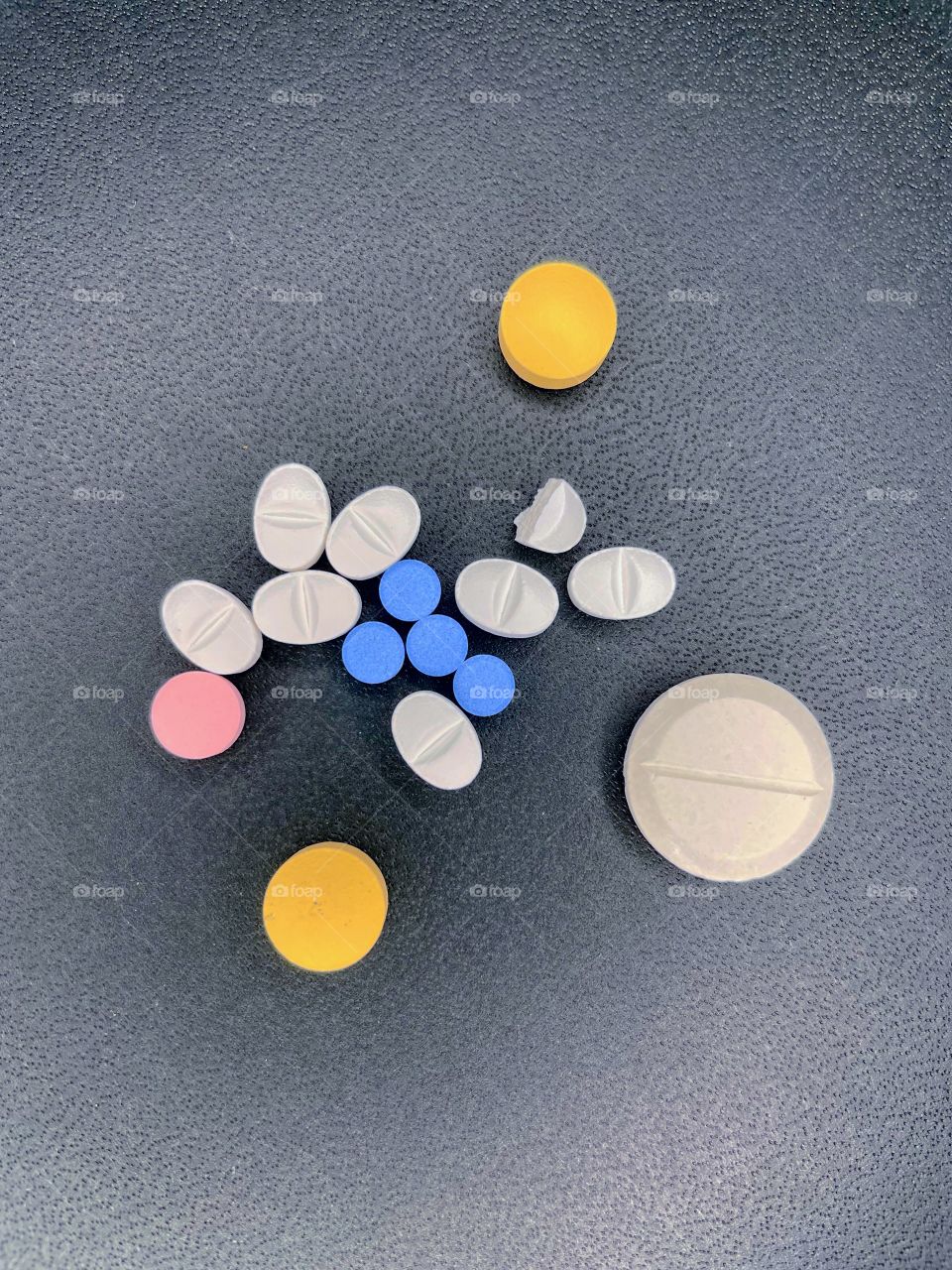 Several pills are scattered on a black background. There are orange, white, pink, and blue pills. 