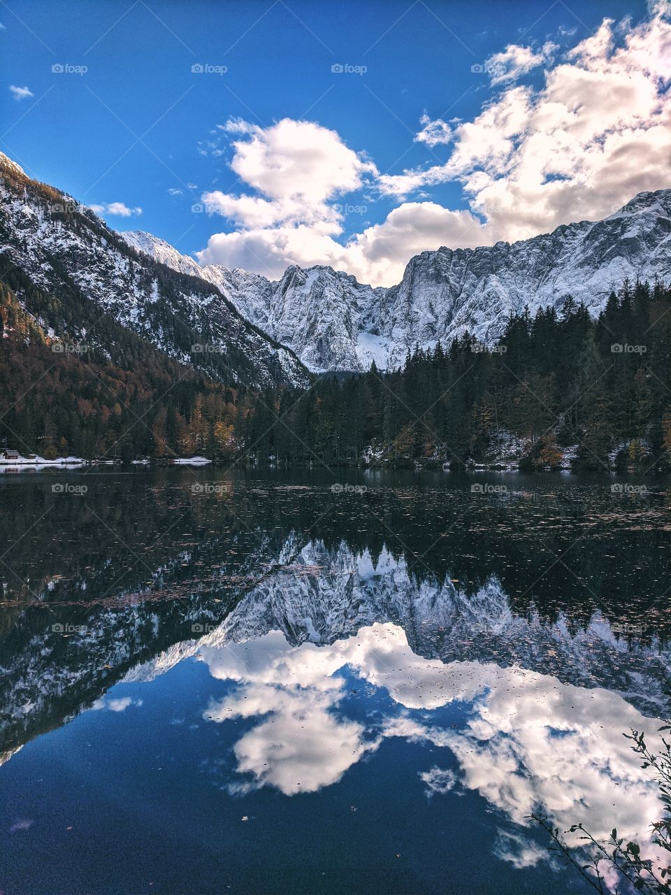 View of the autumn snow-capped mountain peaks against the backdrop of a transparent Italian lake.
