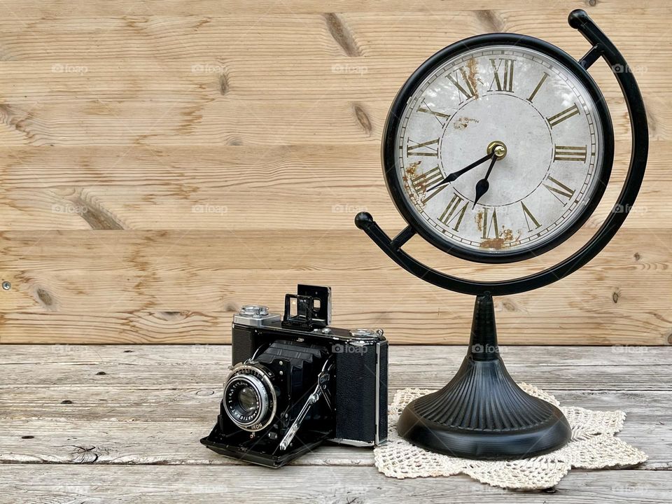 Retro clock and vintage camera on the wooden background 