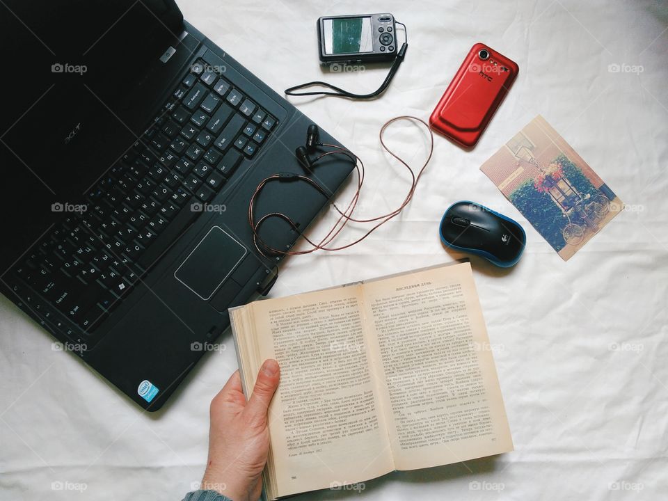 Laptop, book, notebook, red smartphone, computer mouse and camera are lying on the table