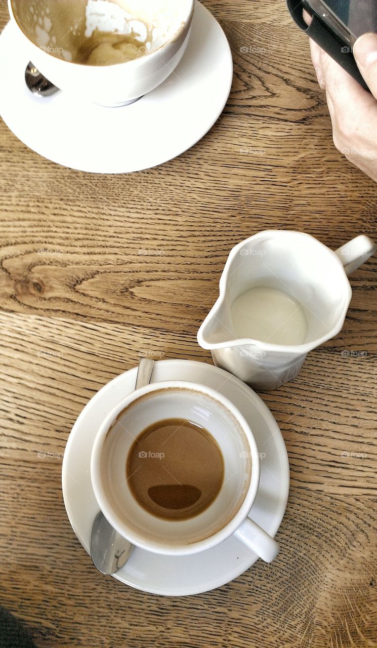 Almost empty cup or coffee and milk jar standing on brown wooden table