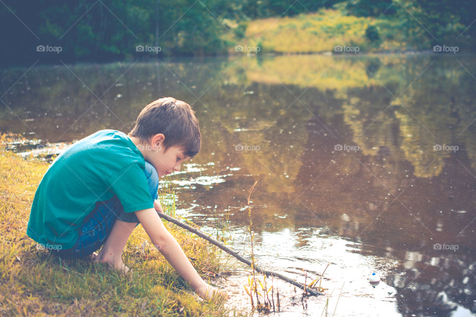 Young Boy Playing in Pond with Stick