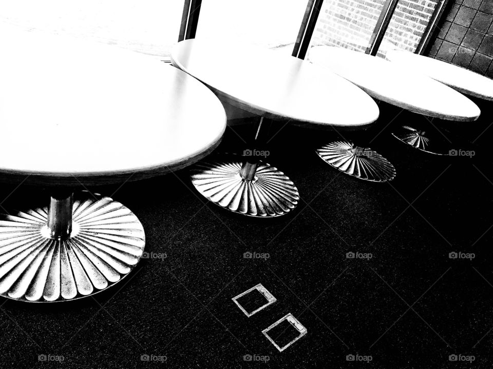 Fun black and white photo of four circular tables lined up against row of windows. 