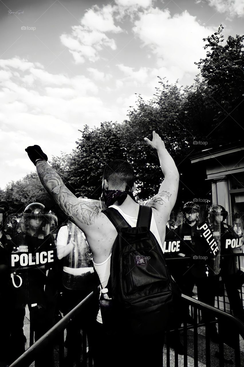 Protester facing police line, black and white
Black and white photo of a protester with arms raised facing police in riot gear.