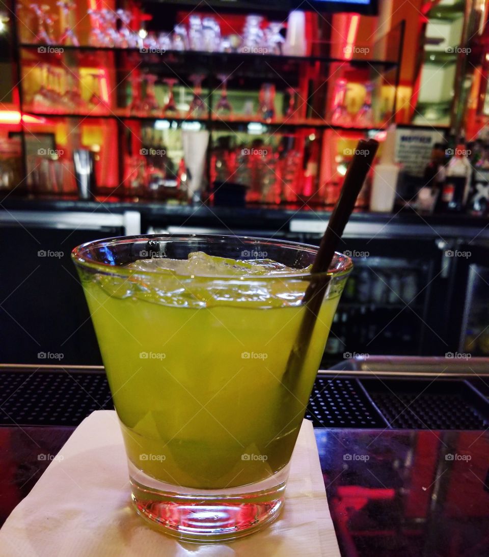 Bright green cocktail in a glass sitting on the counter at a bar at night