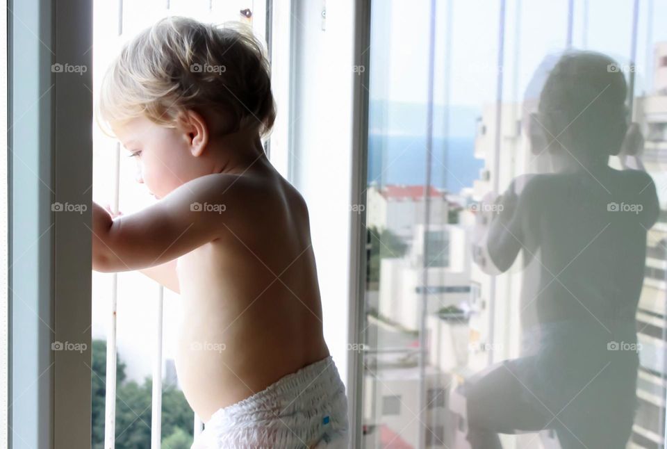 The boy looks out the window and his reflection is visible on the window glass