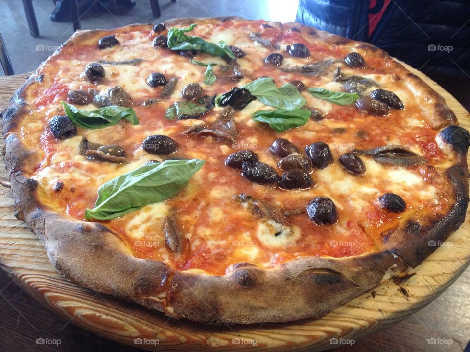 A hand tossed pizza with kalamata olives, anchovies and fresh basil baked in a wood-fired pizza oven.