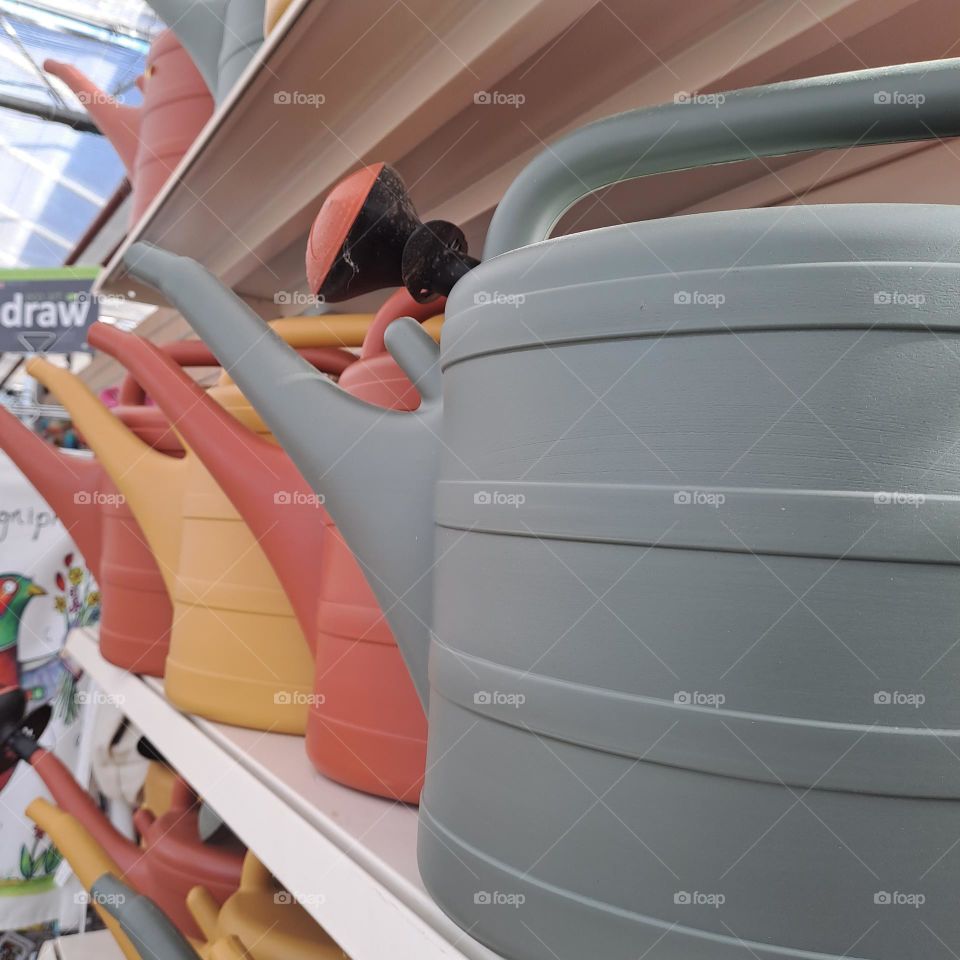 coloured watering cans on a shelf in a shop orange green yellow. gardening. garden
