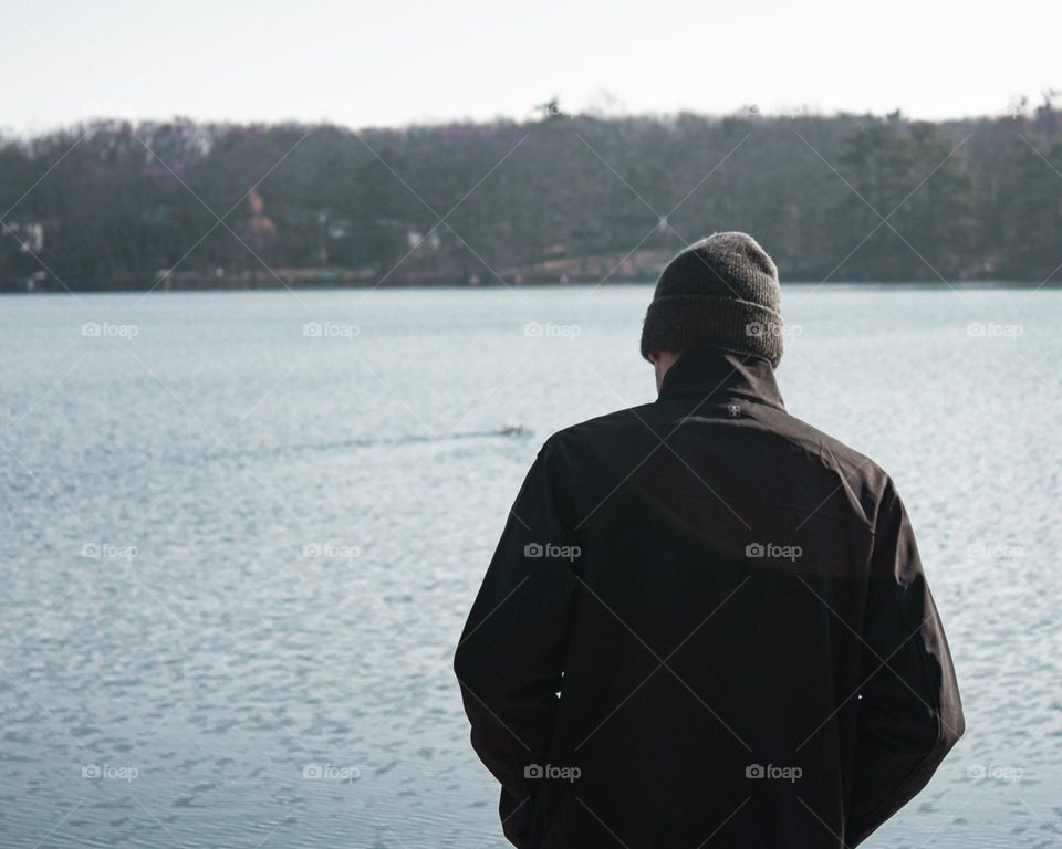 Lightweight jacket and a beanie; Male model standing in front of a body of water