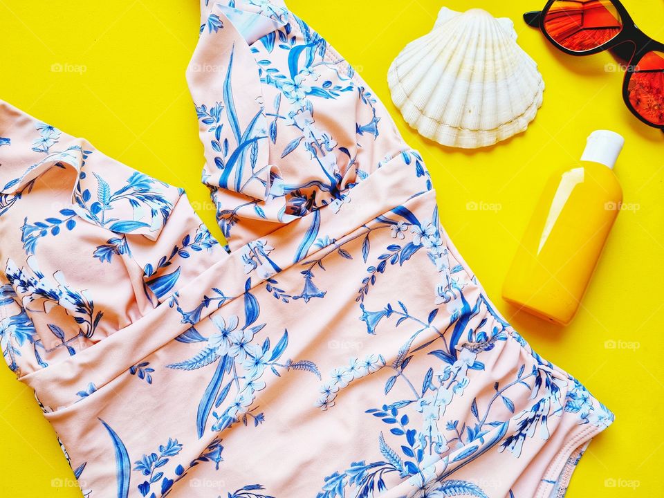 pink one-piece swimsuit and accessories for the sea on a yellow background