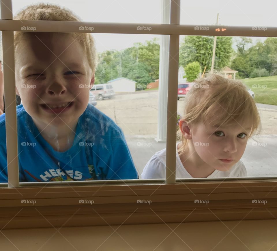 Little boy with his face pressed up against the window and a little girl beside him looking in the window 