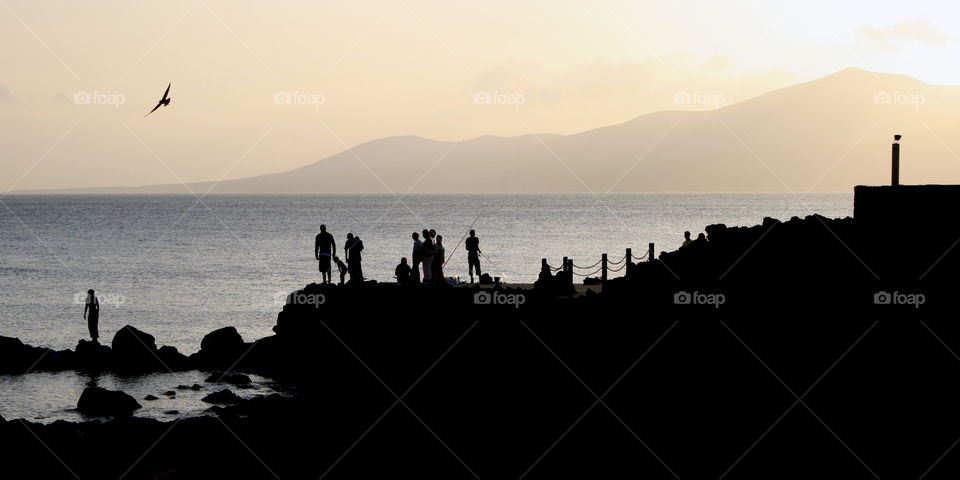 Silhouette of people standing on rock near the sea