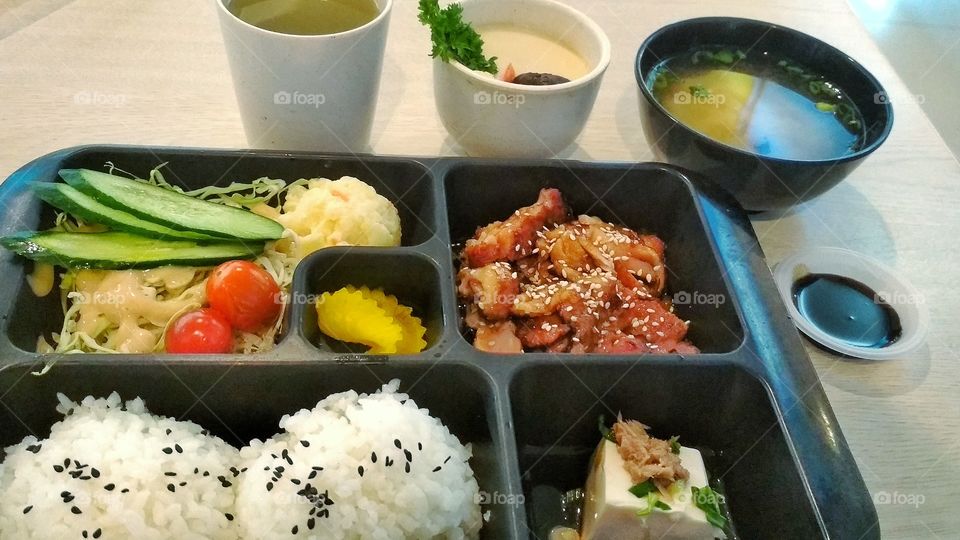 A japanese bento: Rice, tofu, teriyaki chicken, mashed potato; with miso and chawan mushi. Japanese green tea as a drink.