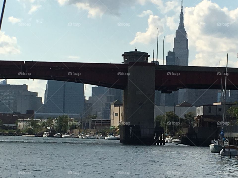 A beautiful view of Newtown Creek, LIC, Queens with its boats and of the Pulaski Bridge. In the far distance you can see the Empire State Building in Manhattan and various buildings in either Queens or Manhattan. 2019. Hypnotic Productions