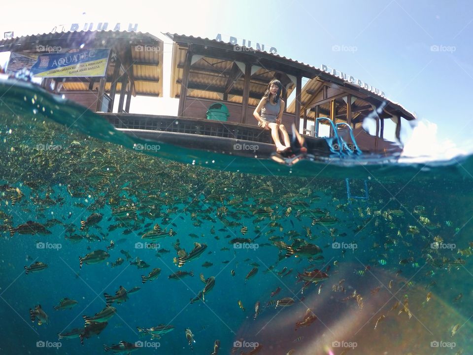 Woman sitting on floating house above school of fish swimming underwater