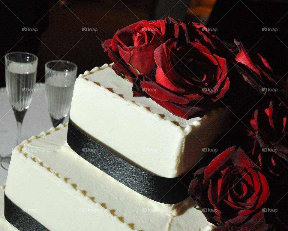 Square white wedding cake with black ribbon and deep red roses cascading from top to bottom 
