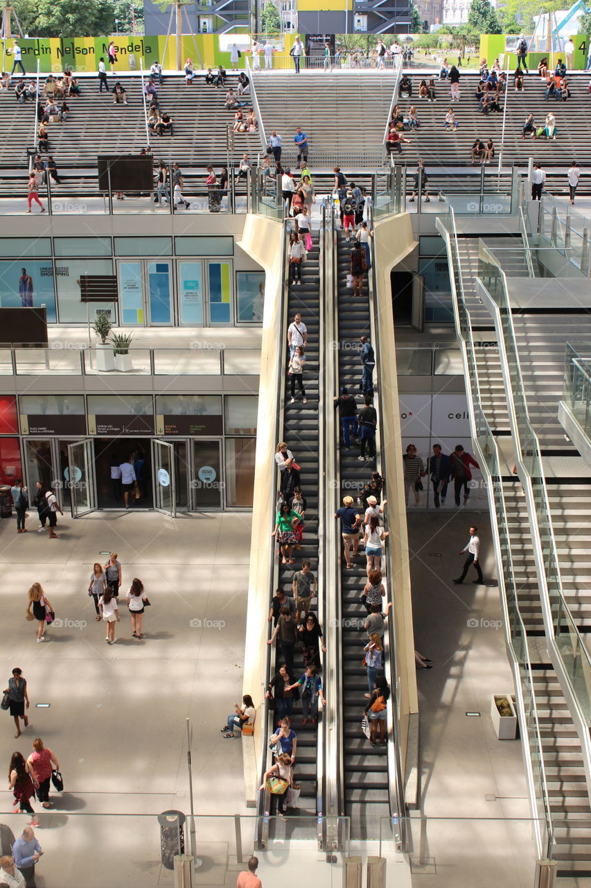 People are using the escalators in a open air shopping center in Paris.