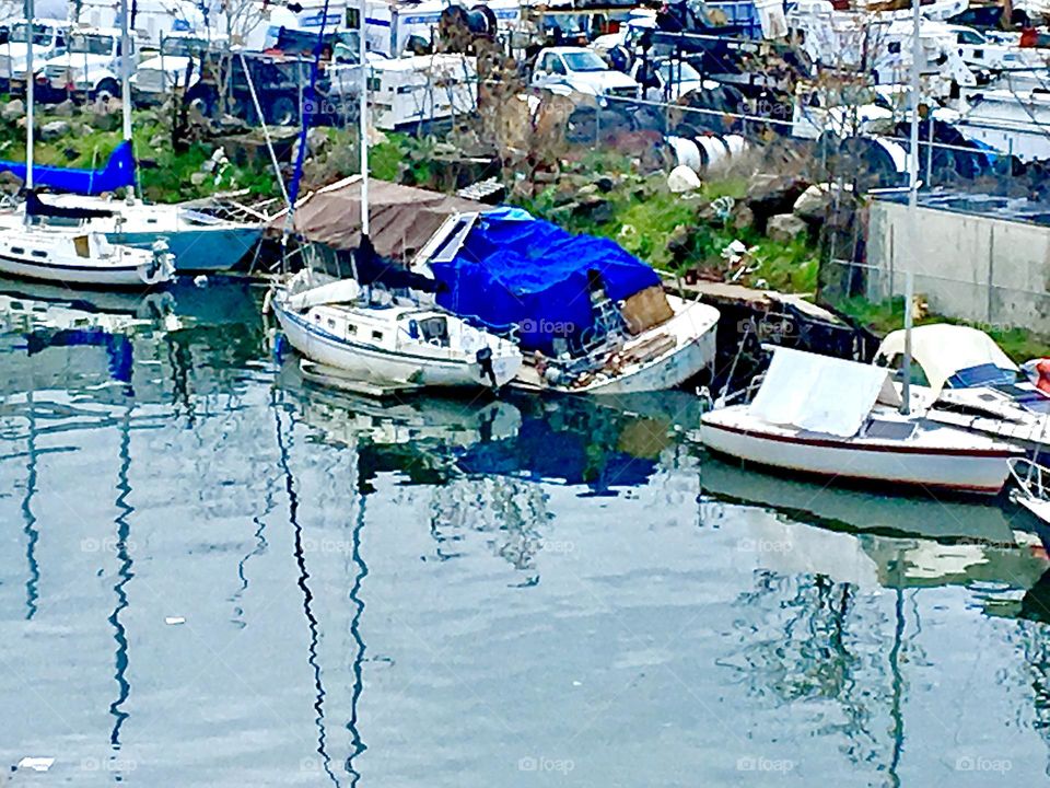 Boats in the waters of the East River at Newtown Creek in Long Island City, Queens, NY close up against the shore at high tide in the summertime of 2021. Through the mesh fence you can see the parking lot. Hypnotic Productions