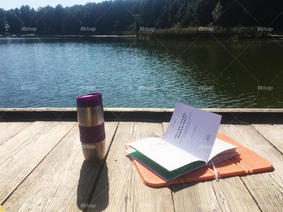 Enjoying coffee in thermo cup reading a book on the river. 