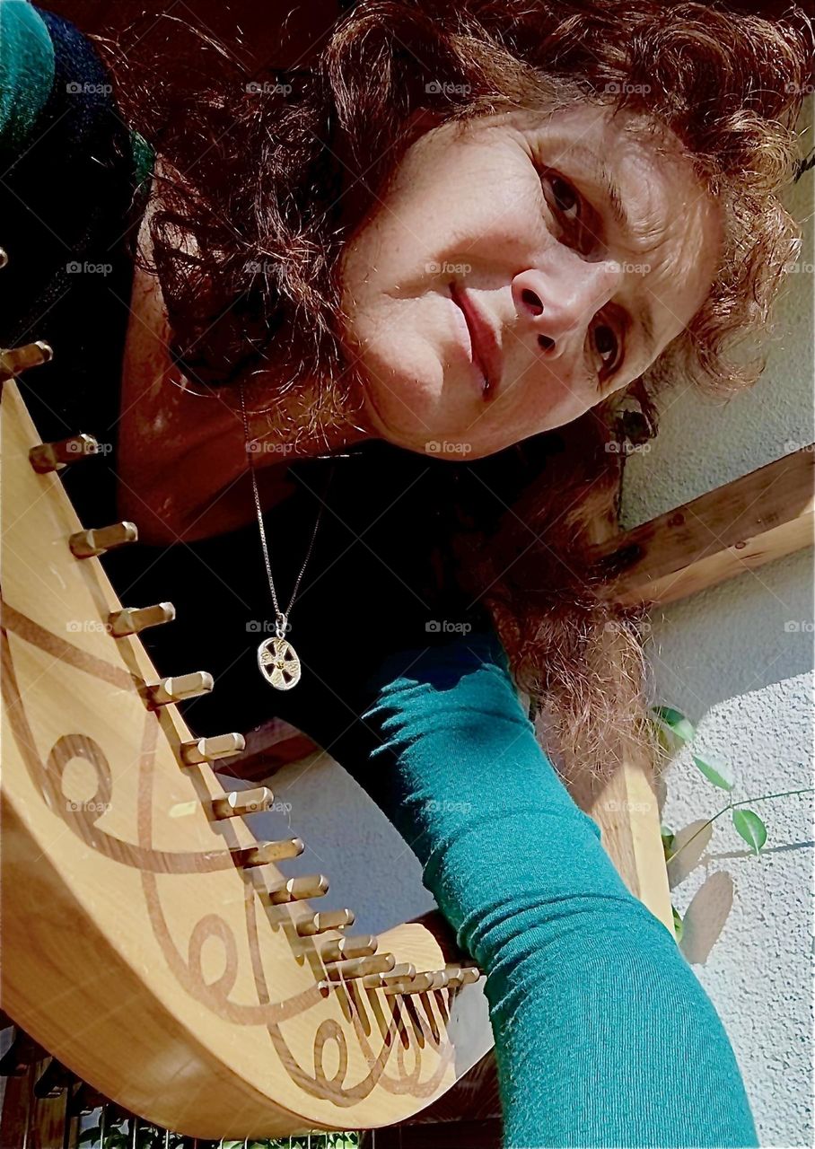 The lovely lady in the green dress with the Celtic silver pendant is holding onto her custom made traditional instrument, the harp while gazing pensively at us. Wonder what she may be thinking … 2023. Hypnotic Productions