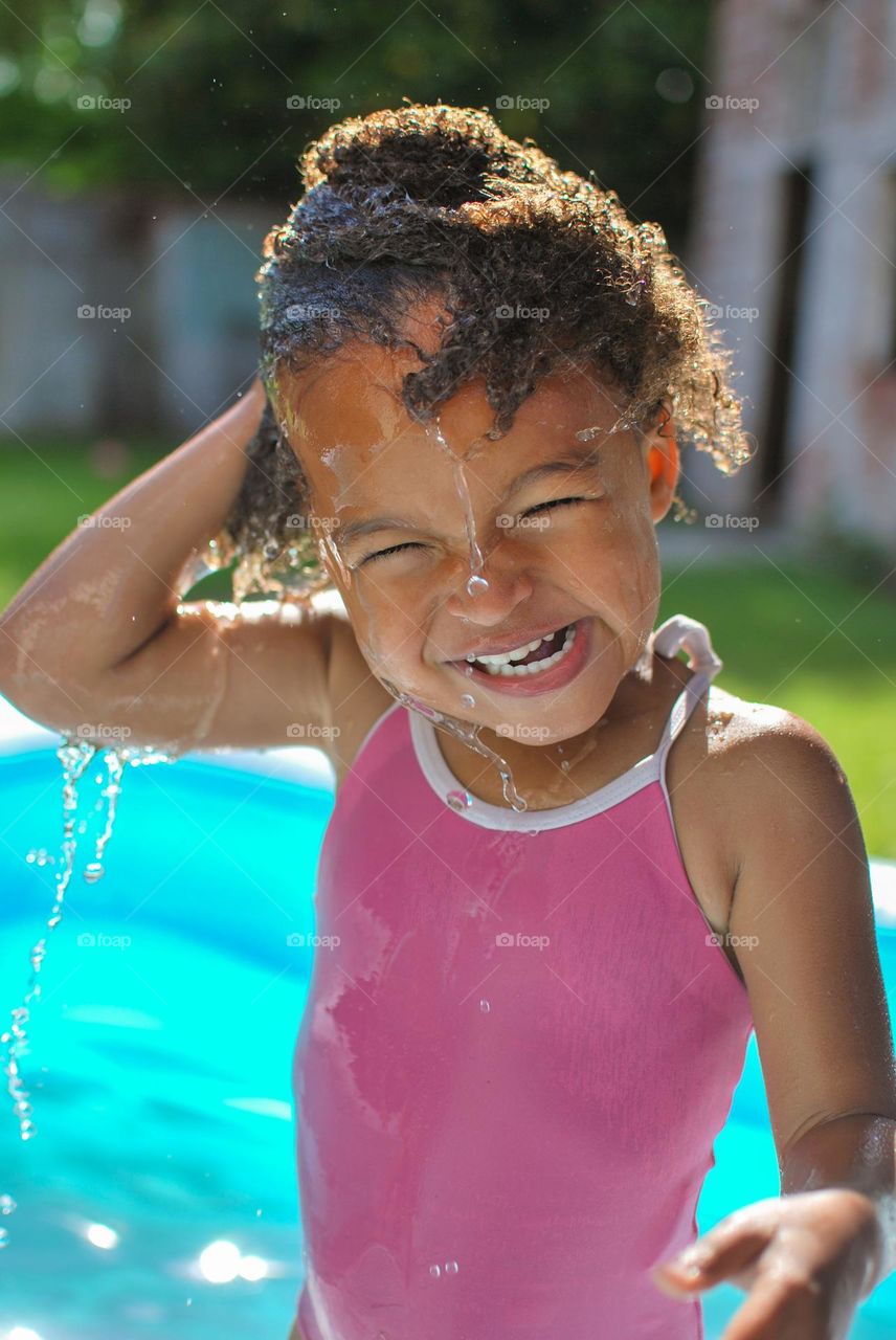 Girl of mixed race enjoying the refreshment of water in a swimming pool on a hot summer day, together with her little sister (family, fun, summer, water, blue, swimming suit, splash, hot, enjoy, play, outdoors)