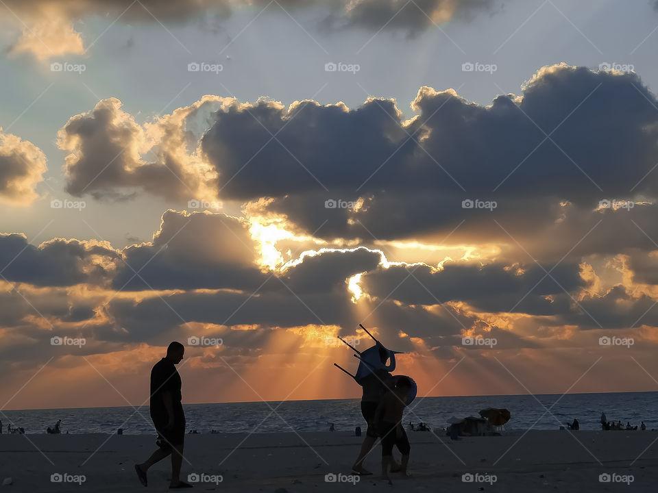 People are walking to the beach at sunset.
