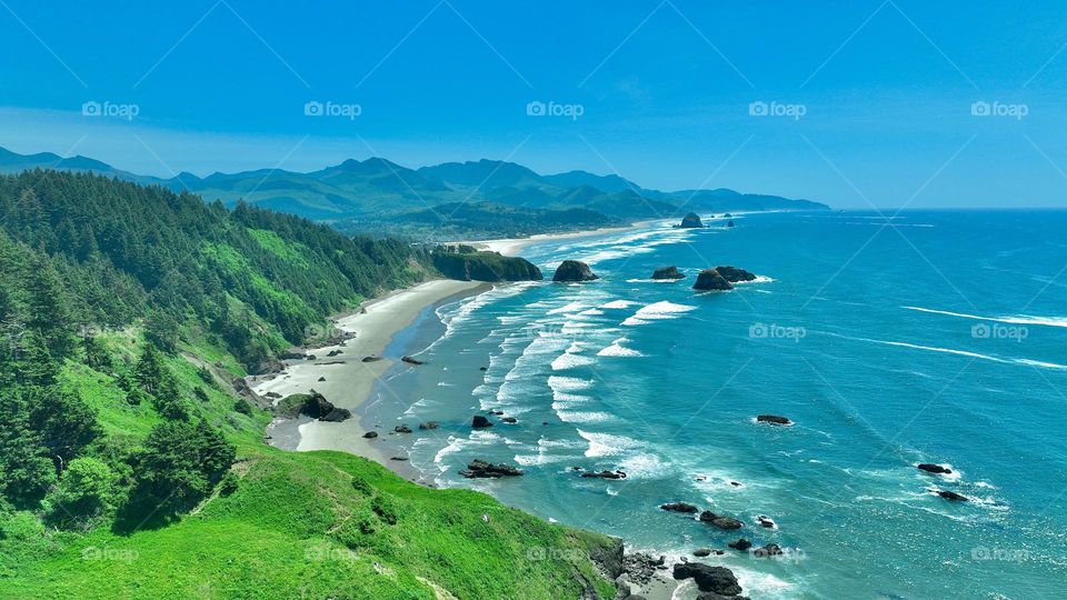 Where the land meets the sea. A beautiful symphony of cascading cliffs, lush green forest, and the majesty of the waves crashing against the rugged shoreline above Ecola State Park in Cannon Beach, Oregon.